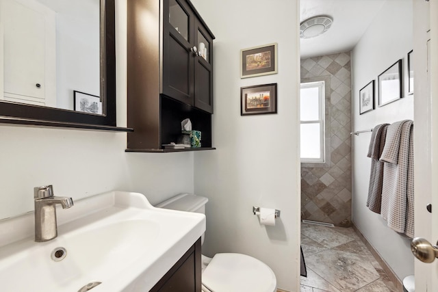 bathroom featuring tiled shower, toilet, and vanity