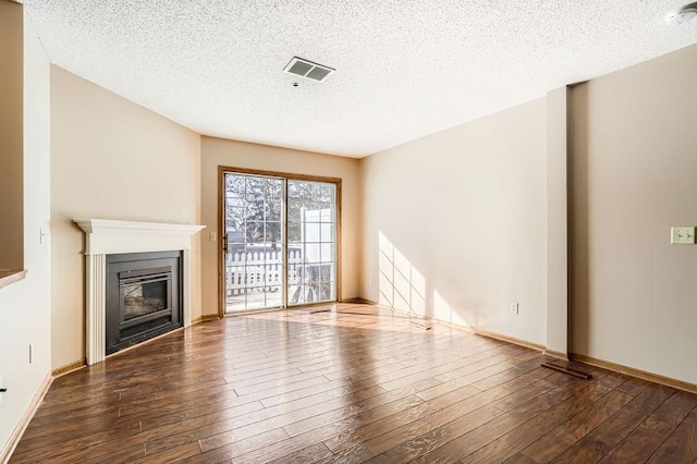 unfurnished living room with a textured ceiling, a glass covered fireplace, wood finished floors, and visible vents