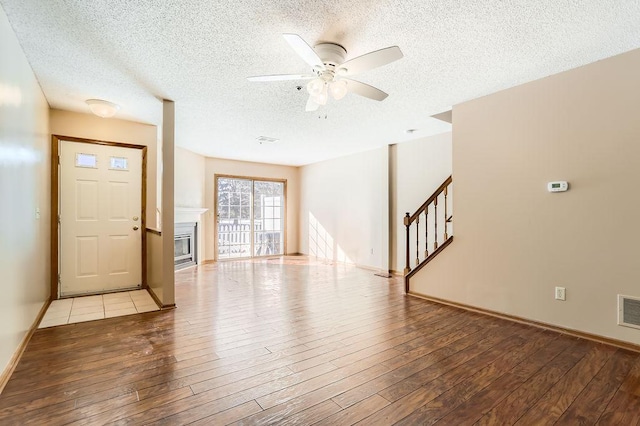 entryway with a textured ceiling, ceiling fan, stairway, light wood-type flooring, and a glass covered fireplace