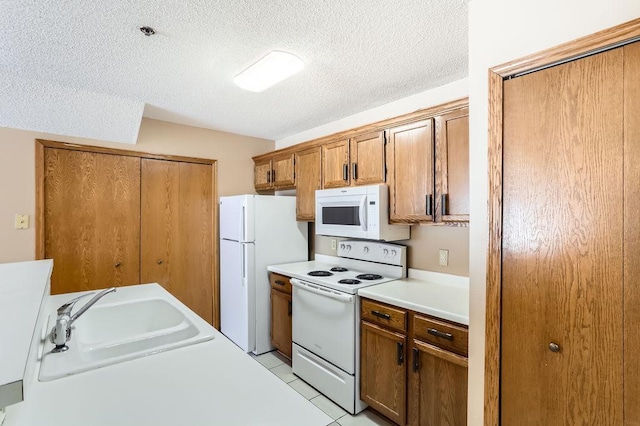 kitchen with white appliances, brown cabinetry, light countertops, a textured ceiling, and a sink