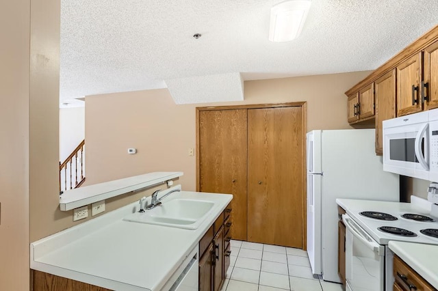 kitchen featuring white appliances, brown cabinetry, light countertops, a textured ceiling, and a sink