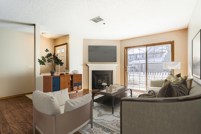 living area with baseboards, visible vents, a glass covered fireplace, dark wood-style floors, and a textured ceiling