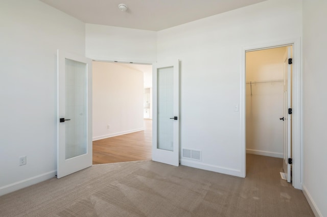 unfurnished bedroom featuring a walk in closet, french doors, light carpet, and visible vents