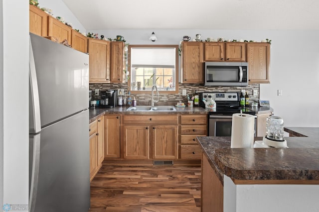 kitchen featuring dark wood-style flooring, dark countertops, backsplash, appliances with stainless steel finishes, and a sink