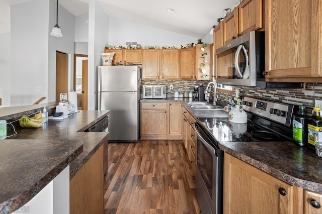 kitchen featuring dark wood finished floors, lofted ceiling, dark countertops, appliances with stainless steel finishes, and a sink