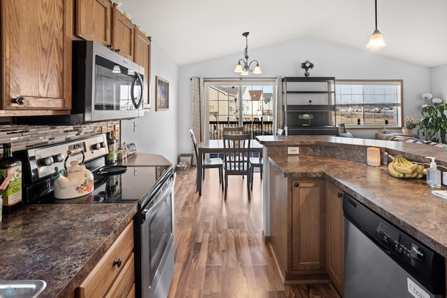 kitchen featuring brown cabinetry, dark countertops, appliances with stainless steel finishes, wood finished floors, and hanging light fixtures