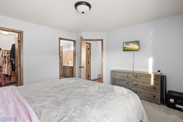 carpeted bedroom with a closet, visible vents, a spacious closet, and ensuite bath