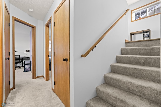 stairway with carpet, baseboards, and a textured ceiling