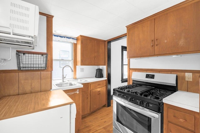 kitchen featuring brown cabinetry, light wood-style flooring, light countertops, a sink, and gas stove