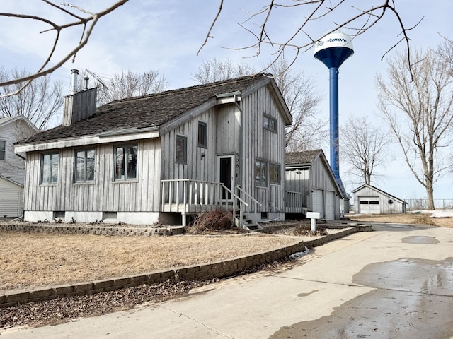 view of front facade featuring an outbuilding, a shingled roof, a chimney, a garage, and board and batten siding