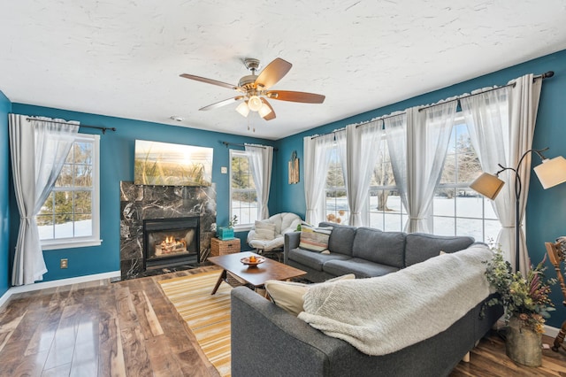 living area featuring a textured ceiling, a fireplace with flush hearth, wood finished floors, a ceiling fan, and baseboards