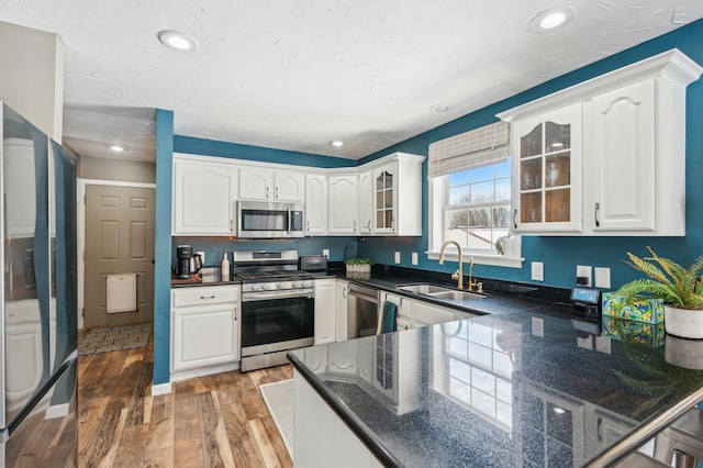 kitchen with stainless steel appliances, light wood-style floors, glass insert cabinets, white cabinetry, and a sink