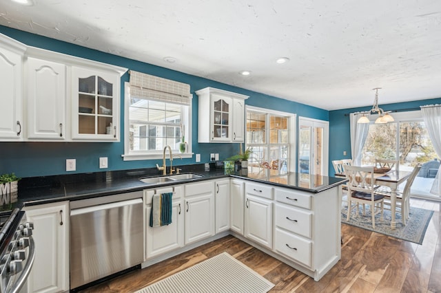 kitchen with stainless steel appliances, a peninsula, a sink, dark countertops, and glass insert cabinets