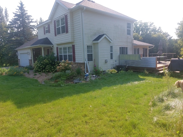 view of side of home featuring an attached garage, stone siding, a deck, and a yard