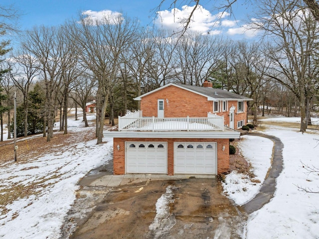 snow covered property with driveway, brick siding, and a chimney