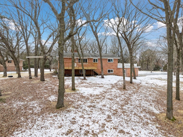 snow covered property featuring brick siding and a wooden deck