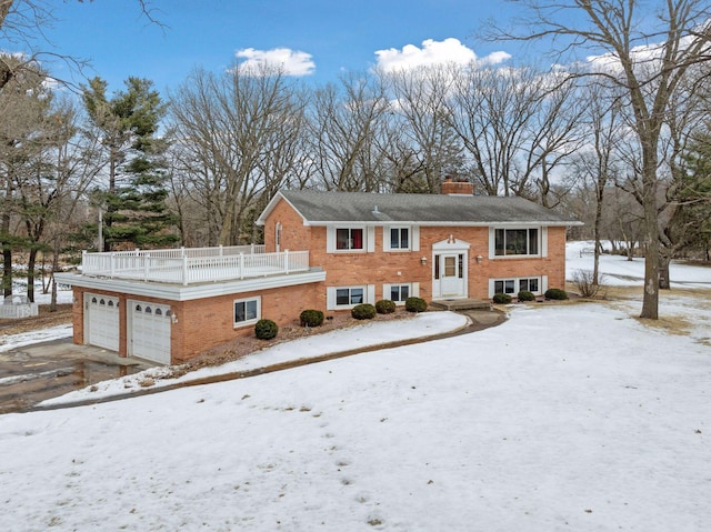 snow covered rear of property featuring a garage, brick siding, driveway, and a chimney