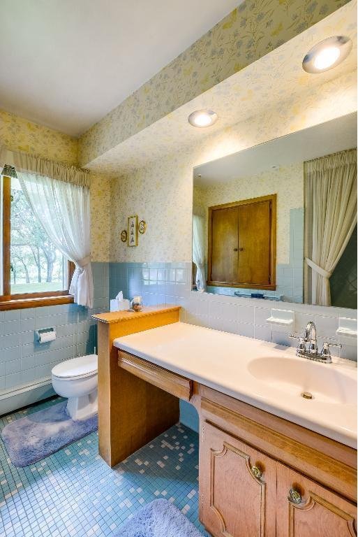 bathroom featuring toilet, wallpapered walls, tile walls, wainscoting, and tile patterned flooring