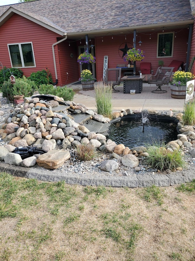 rear view of property featuring a garden pond, a fire pit, and a patio area