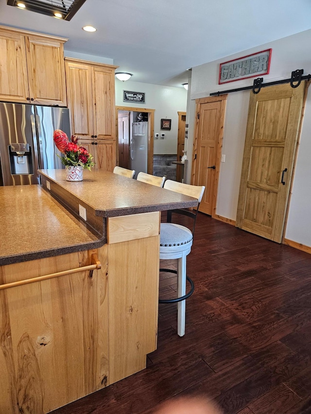 kitchen featuring dark hardwood / wood-style floors, stainless steel fridge with ice dispenser, light brown cabinets, a barn door, and a kitchen bar