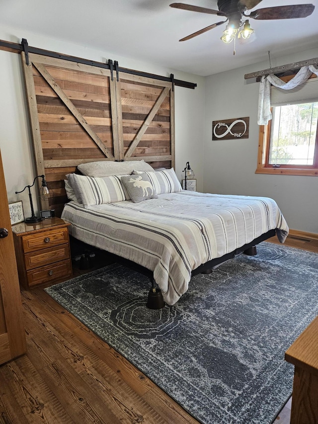 bedroom featuring ceiling fan, a barn door, and dark hardwood / wood-style floors