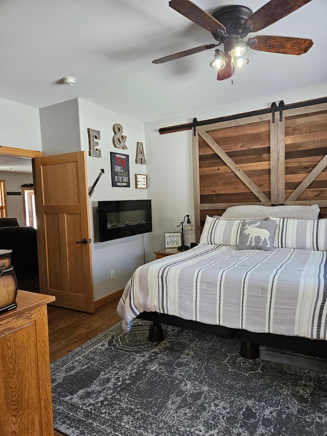 bedroom with ceiling fan, dark wood-type flooring, and a barn door