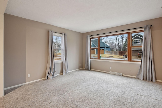 spare room with carpet, a textured ceiling, visible vents, and baseboards