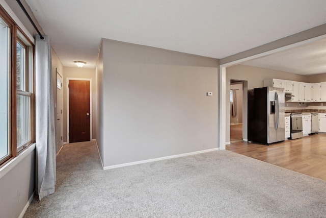 unfurnished living room featuring light colored carpet and baseboards