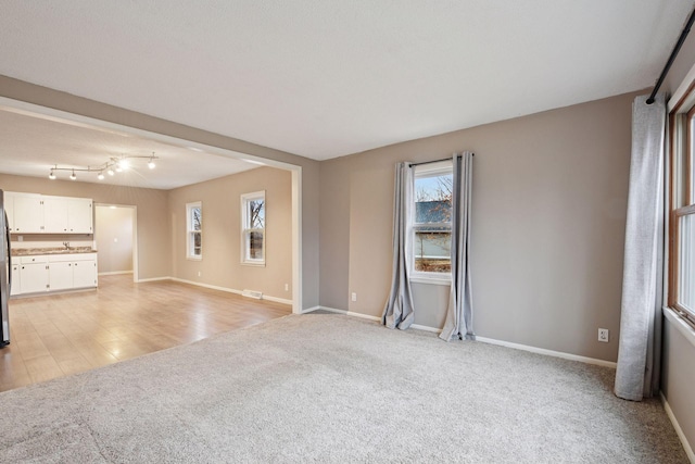 unfurnished living room featuring light carpet, a sink, and baseboards