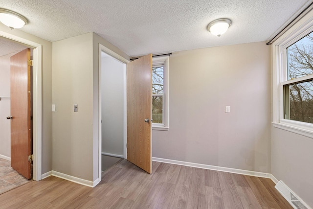 interior space with light wood-style floors, baseboards, visible vents, and a textured ceiling