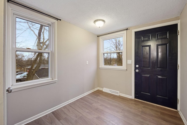 foyer with baseboards, a textured ceiling, visible vents, and wood finished floors