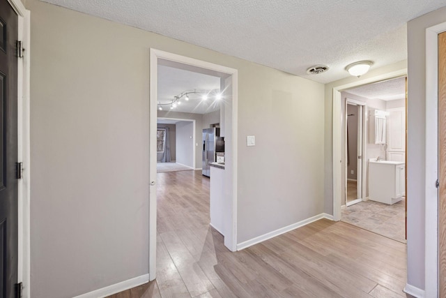 hall with a textured ceiling, light wood-type flooring, visible vents, and baseboards