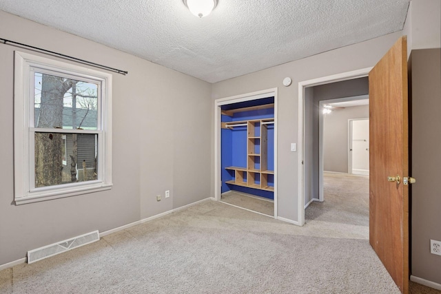 empty room featuring carpet, visible vents, a textured ceiling, and baseboards