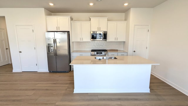 kitchen featuring a kitchen island with sink, decorative backsplash, light countertops, appliances with stainless steel finishes, and white cabinetry