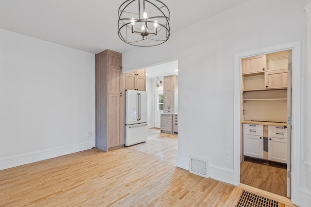 unfurnished dining area with light wood-type flooring, an inviting chandelier, baseboards, and visible vents