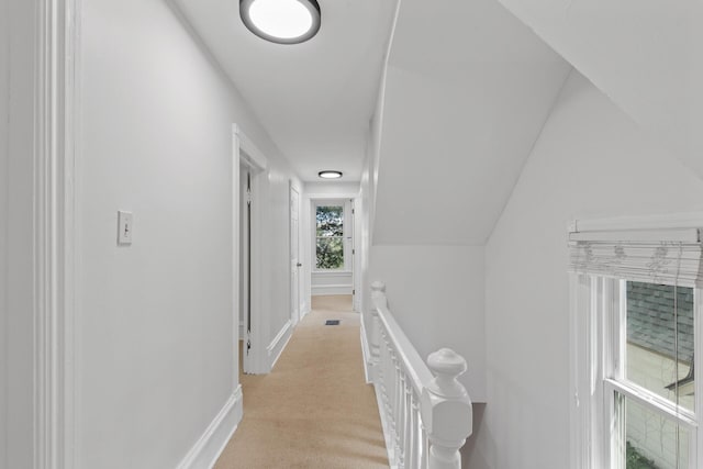 hall with lofted ceiling, baseboards, light colored carpet, and an upstairs landing