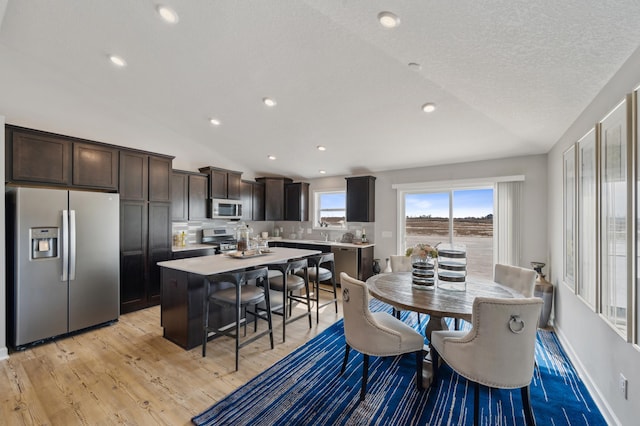 dining area with light hardwood / wood-style floors, lofted ceiling, and a textured ceiling