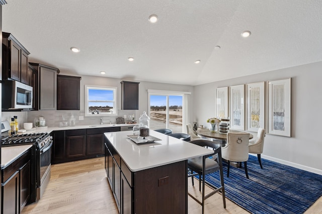 kitchen featuring appliances with stainless steel finishes, a breakfast bar area, light hardwood / wood-style floors, a center island, and sink