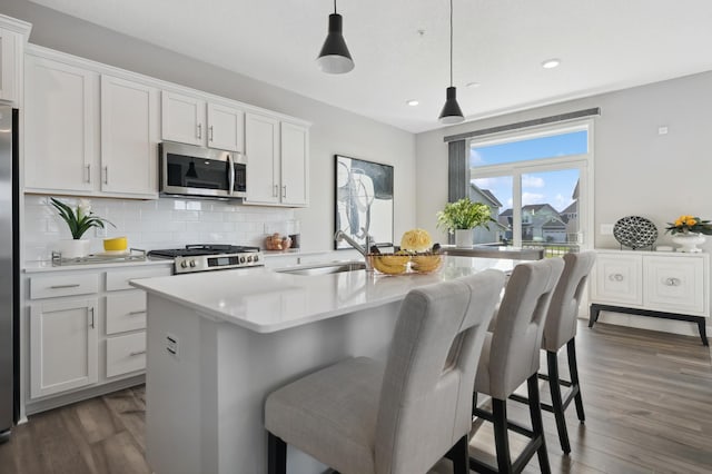 kitchen with a center island with sink, stove, decorative light fixtures, sink, and white cabinetry