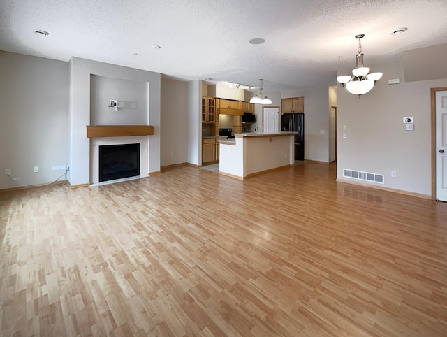 unfurnished living room with a notable chandelier, light hardwood / wood-style flooring, and a textured ceiling