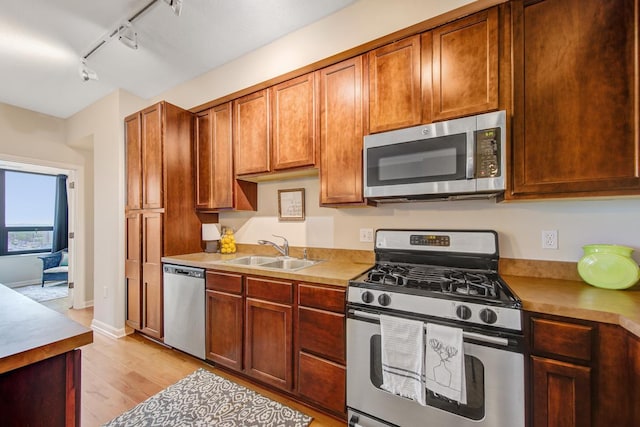 kitchen featuring sink, appliances with stainless steel finishes, rail lighting, and light wood-type flooring