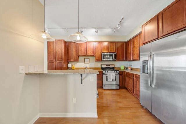 kitchen with appliances with stainless steel finishes, a breakfast bar, light hardwood / wood-style flooring, decorative light fixtures, and kitchen peninsula