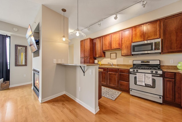 kitchen with appliances with stainless steel finishes, light hardwood / wood-style flooring, hanging light fixtures, a breakfast bar area, and kitchen peninsula