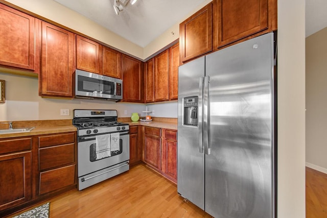 kitchen with appliances with stainless steel finishes, sink, and light hardwood / wood-style floors