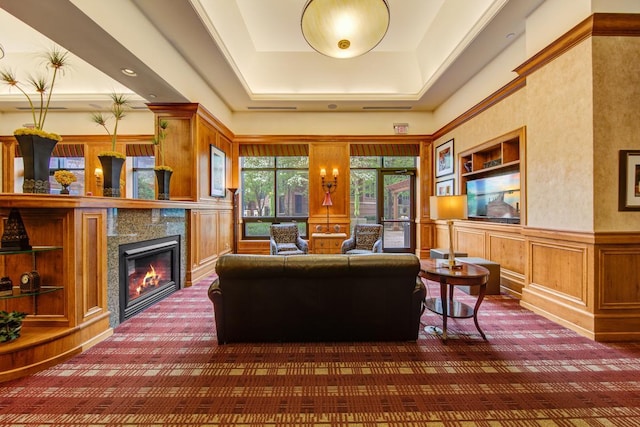 carpeted living room with a tiled fireplace, a raised ceiling, and built in features