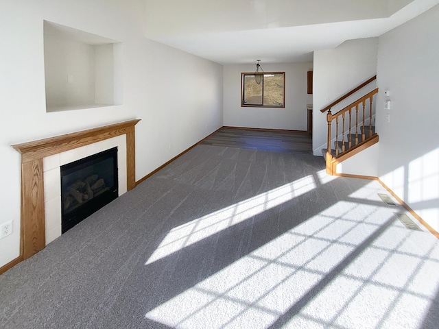 unfurnished living room with carpet, stairs, baseboards, and a glass covered fireplace