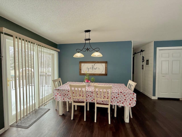 dining space with a textured ceiling, a barn door, and dark hardwood / wood-style floors