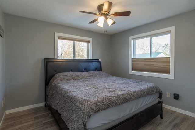 bedroom with ceiling fan, multiple windows, baseboards, and wood finished floors