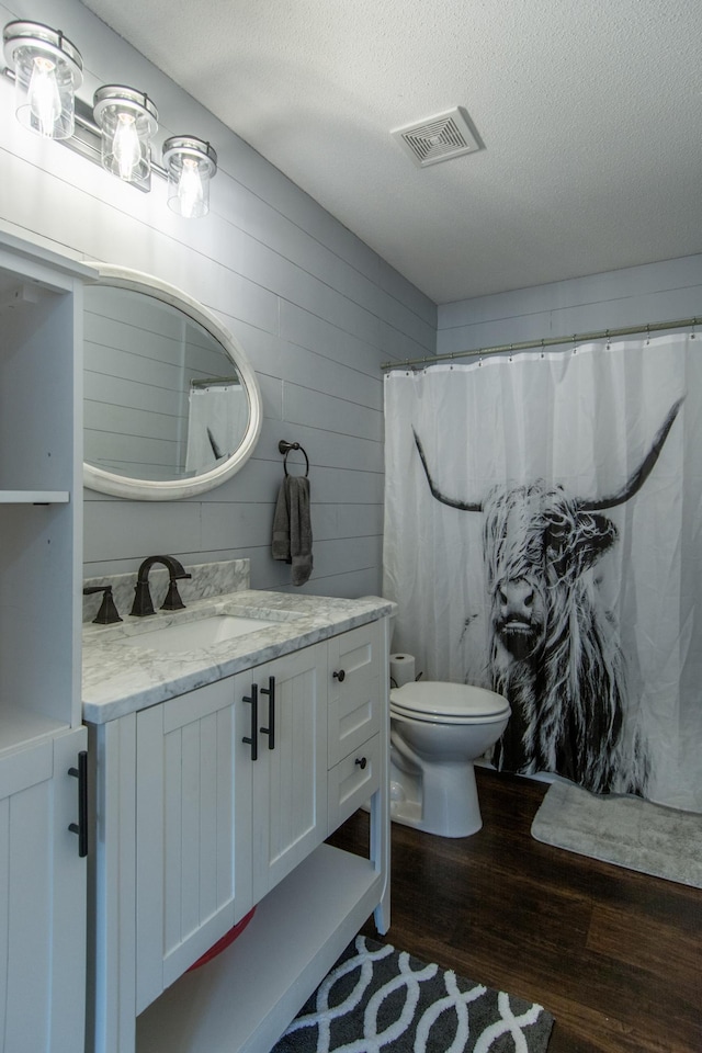 full bath featuring visible vents, toilet, a textured ceiling, vanity, and wood finished floors