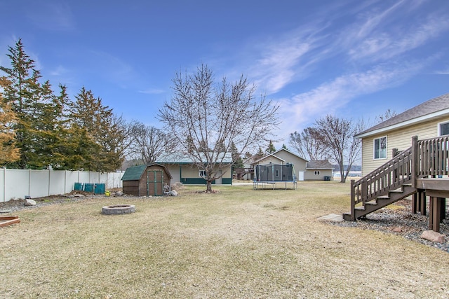 view of yard featuring a trampoline, a fire pit, a shed, a fenced backyard, and an outbuilding